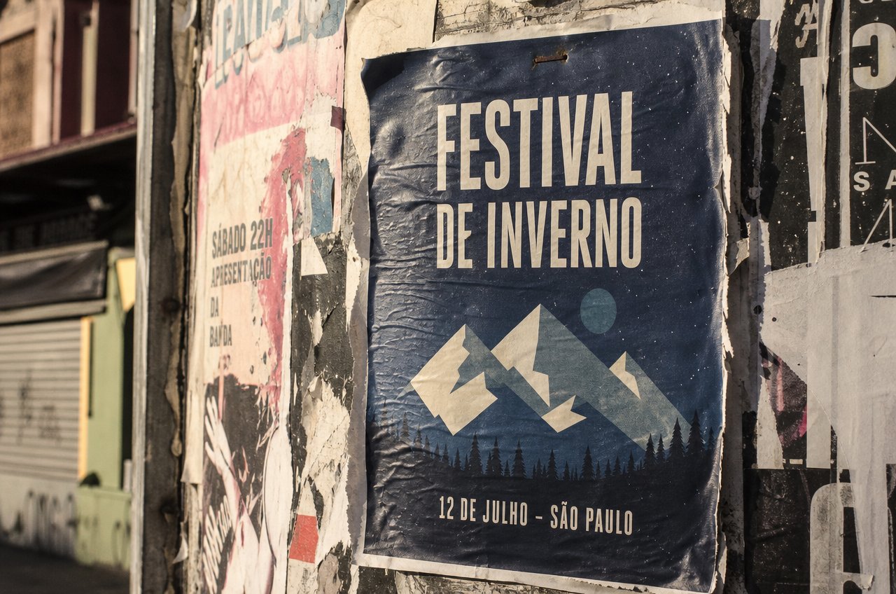 A printed festival poster pasted on a flyer-covered wall, with legible text